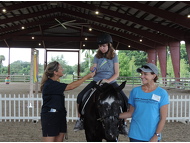 SI member, Renee McCabe Johnson and Equine-Assisted Therapies volunteer, Daniela present a ribbon to rider, Cassidy G.and horse, Sugar.